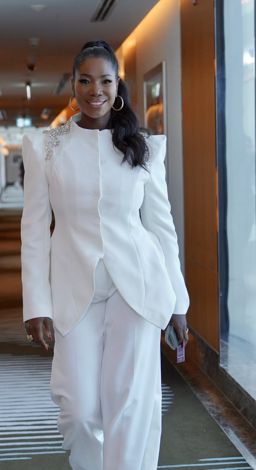 Ellen Mannaert in a white tailored suit, walking through a hotel corridor